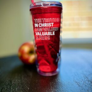 A red cup with an apple and water on the table.