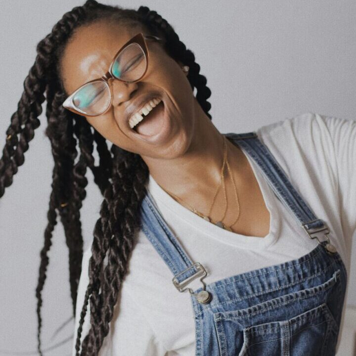 A woman with glasses and braids is smiling.